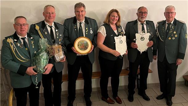 Sechs Mitglieder des Schützenvereins in grünen Uniformjacken stehen nebeneinander und präsentieren ihre Auszeichnungen. Zwei Personen halten bemalte Holzscheiben, andere haben Geschenke in den Händen.