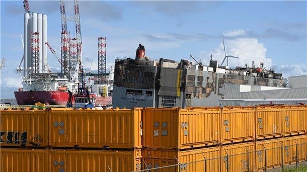 Der schwer beschädigte Autofrachter „Fremantle Highway„ wird durch gelbe Container abgeschirmt.