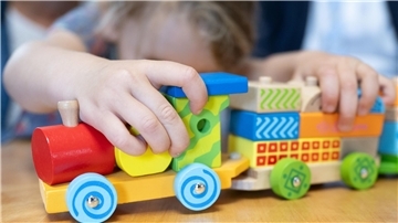Kinderhände schieben einen Holzzug.