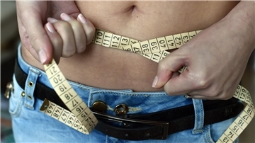 Eine junge Frau legt ein Maßband um ihren Bauch