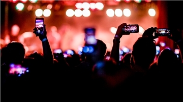 Fans filmen mit Smartphones aus dem Publikum heraus ein Konzert.