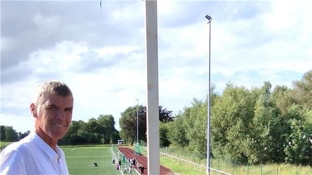Ein Mann steht oberhalb eines Fußballplatzes und lächelt.