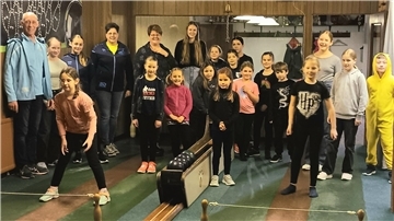 Eine Gruppe Kinder und Jugendliche steht auf einer Kegelbahn.