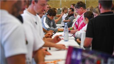 Menschen in einer Sporthalle geben Autogramme. 