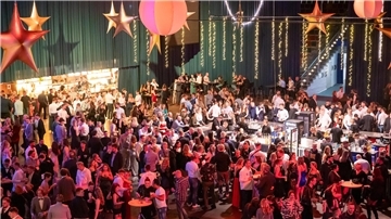 Viele Menschen stehen in einer weihnachtlich geschmückten Halle und feiern.