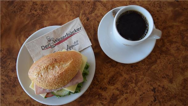 Brötchen am Feiertag: Zu diesen Zeiten haben die Bäckereien in der Wesermarsch geöffnet Es ist ein Brötchen zu sehen, das auf einem Teller angerichtet wurde. Daneben steht ein Becher Kaffee.