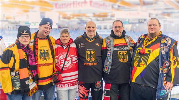 Eine Gruppe von Männern und Frauen mit verschiedenen Eishockey-Trikosts, Schals und Mützen.  Gemeinsam für den Eishockey-Sport – Rita, Andreas, Conny, Mario, Oliver und Gerald genießen die Atmosphäre in der Eisarena.