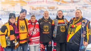 Eine Gruppe von Männern und Frauen mit verschiedenen Eishockey-Trikosts, Schals und Mützen.  Gemeinsam für den Eishockey-Sport – Rita, Andreas, Conny, Mario, Oliver und Gerald genießen die Atmosphäre in der Eisarena.