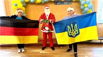 Zwei Frauen halten die deutsche beziehungsweise ukrainische Flagge in ihren Händen, dazwischen steht ein als Weihnachtsmann verkleideter Mann.
