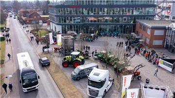 Eine Luftaufnahme von einem Firmengelände zeigt im Halbrund zur Präsentation geparkte Landmaschinen, Lkw und Nutzfahrzeuge. Besuchergruppen laufen zwischendurch.