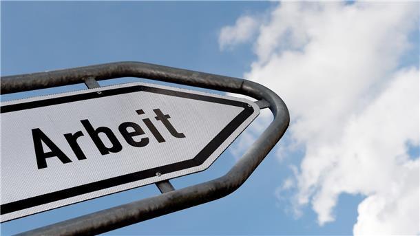 Ein Hinweisschild mit der Auschrift "Arbeit" ragt gen Himmel.