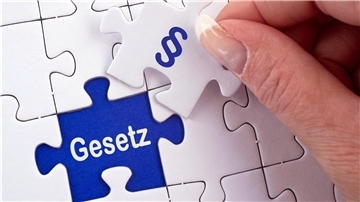 Eine Hand hält ein Puzzleteil mit der Aufschrift "Gesetz".