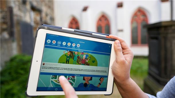 Ein Mann zeigt auf einem Tablet die App "Dorffunk".