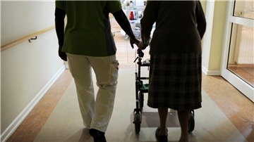 Eine Pflegekraft läuft neben einer Frau mit Rollator.