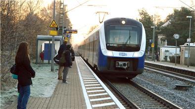 Eine Bahn hält am Bahnhof, an dem Menschen warten. 