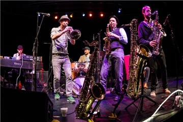 Fünf Musiker auf der Bühne mit Saxofon, Trompete, am Schlagzeug und Keyboard