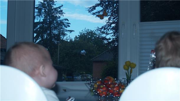 Zwei Kinder sitzen an einem Tisch vor einem Fenster mit Einschussloch.