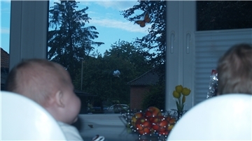 Zwei Kinder sitzen an einem Tisch vor einem Fenster mit Einschussloch.