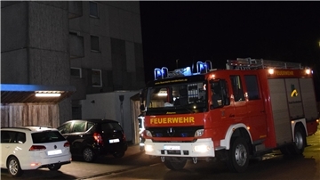 Feuerwehrauto steht vor einem Hochhaus, daneben sind zwei Autos zu sehen.