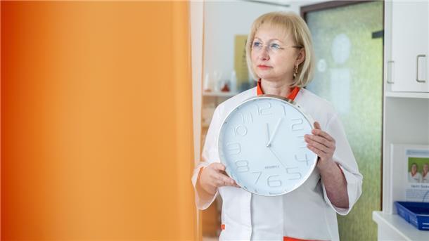 Die Ärztin hält eine Uhr in der Hand, die 12.05 Uhr anzeigt.