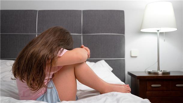 Ein Kind sitzt weinend auf einem Bett. 