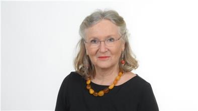 Autorin Monika Kiel-Hinrichsen: graue schulterlange Haare, Brille, ernter Blick. Schwarzes Oberteil, Bernsteinkette