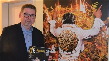 Ein Mann mit einem Magazin in der Hand steht neben einem großen Elvis-Bild.