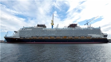 Das Kreuzfahrtschiff „Disney Adventure“ liegt während der Bauphase im Hafen; sichtbare Gerüste, Kräne und Ausrüstung zeugen von laufenden Arbeiten am Schiff.