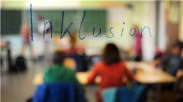 Schüler sitzen in einem Klassenraum unter einem Schriftzug "Inklusion", Aufnahme durch eine beschriebene Glasscheibe hindurch