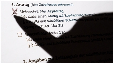 Silhouette einer Hand mit Stift macht ein Kreuz auf dem Formular eines Asylantrags