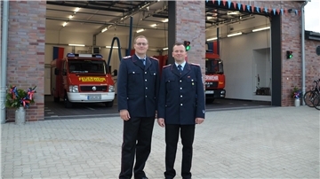 2 Männer in Uniform vor Haus mit Feuerwehrfahrzeugen