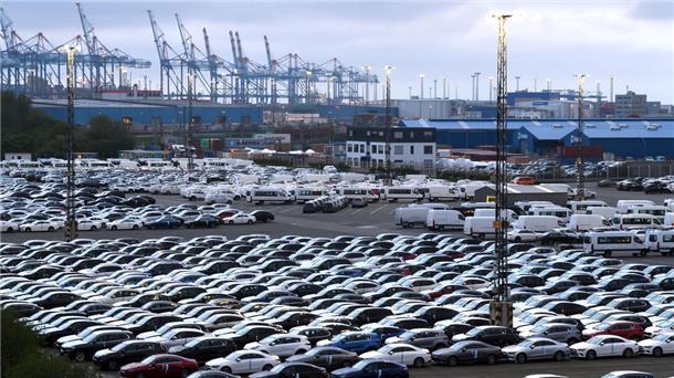 Geparkte Autos und Containerbrücken im Hintergrund.