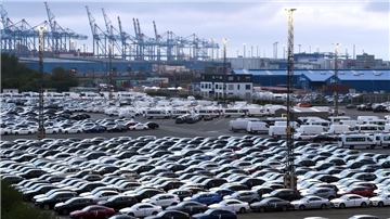 Geparkte Autos und Containerbrücken im Hintergrund.