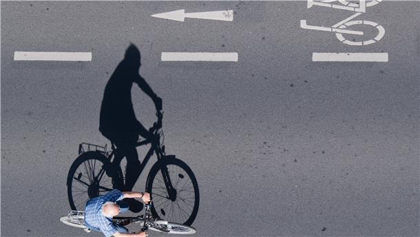 Der Schatten eines Radfahrers ist auf dem Asphalt der Straße zu sehen.