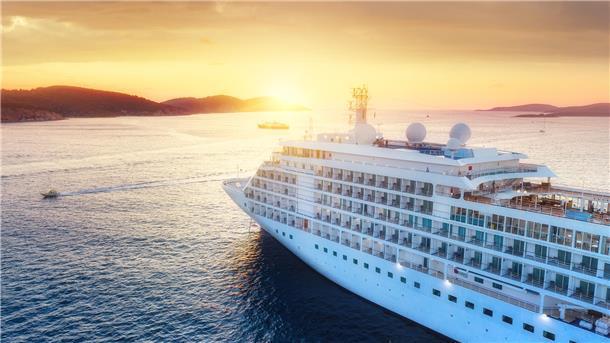 Ein Kreuzfahrtschiff fährt auf dem Meer vor einem Sonnenuntergang.