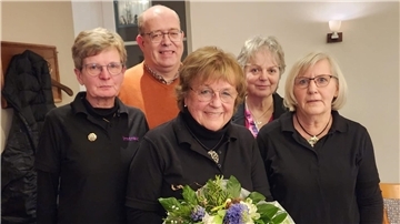 Vier Frauen und ein Mann lächeln in die Kamera. Eine Frau hat einen Blumenstrauß in der Hand.