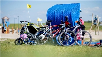 Die Fahrräder einer Familie lehnen am Friesenstrand im Landkreis Wesermarsch an einem blauen Strandkorb.