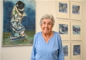 Eine Frau steht vor einer mit Bildern behängten Wand.