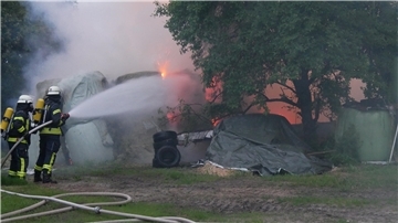 Feuerwehrleute halten einen Schlauch und richten den Wasserstrahl auf Flammen. 
