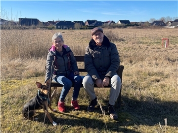 Paar mit Hund sitzt auf einer Bank.