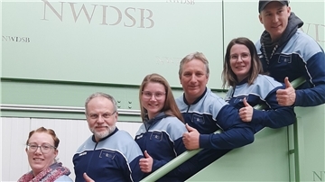 Sechs Menschen stehen auf einer Treppe und zeigen "Daumen hoch".