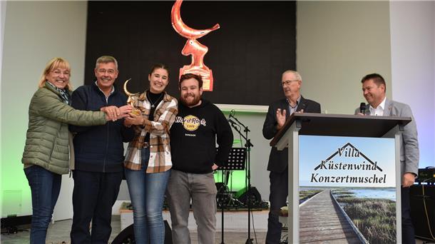 Damen und Herren stehen auf einer Bühne und halten die goldene Krabbe in die Luft. 