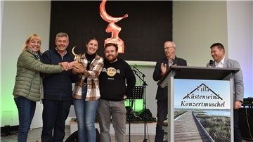 Damen und Herren stehen auf einer Bühne und halten die goldene Krabbe in die Luft. 