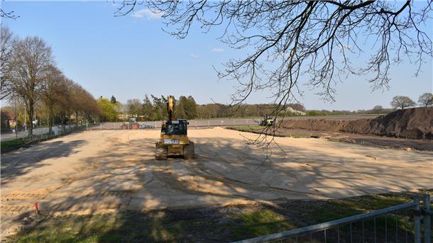 Ein Bagger fährt über eine Sandfläche.