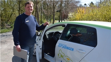 Ein Mann steht an einem Auto, bei dem die Fahrertür geöffnet ist.