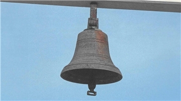 Man sieht eine alte Messingglocke vor blauem Hintergrund.