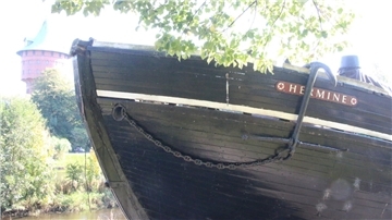 Die „Hermine“ liegt im Sonnenlicht am Schleusenpriel und verfällt zusehends – das marode Holzschiff ist längst kein Aushängeschild der Stadt mehr, sondern ein Sinnbild kommunaler Vernachlässigung.