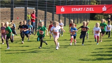 Junge Läuferinnen und Läufer sprinten über einen Rasen.
