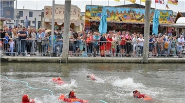 Menschen schwimmen vor Publikum im Wasser.
