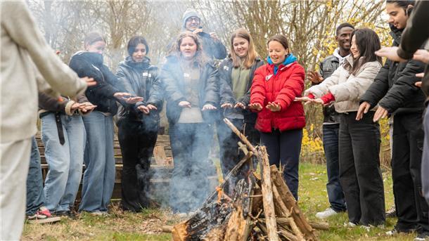 Jugendliche halten ihre Hände zum Lagerfeuer und singen.